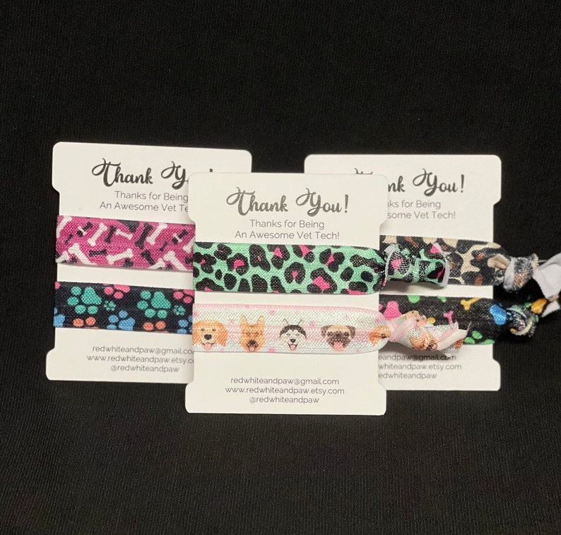 Op de afbeelding: Drie sets met kleurrijke haarbandjes met hondenthema's. Elke set bevat drie haarbandjes met verschillende ontwerpen. De haarbandjes zijn verpakt op witte kaartjes met de tekst "Bedankt! Bedankt dat je een geweldige dierenartsassistent bent!" en contactgegevens van de verkoper.