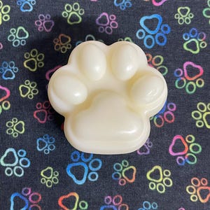May include: A white paw-shaped soap bar on a black background with colorful paw prints.
