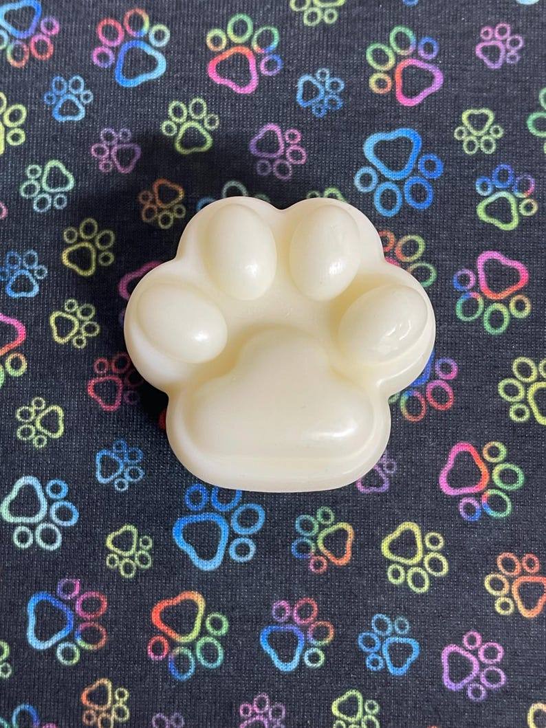 May include: A white paw-shaped soap bar on a black background with colorful paw prints.