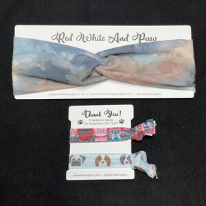 May include: A set of two colorful hair ties with a dog print design. The hair ties are packaged on a white card with the text "Red White And Paw" and "Thank You! Thanks for Being An Awesome Vet Tech!" The card also includes the website address "redwhiteandpaw.com" and the social media handle "@redwhiteandpaw".
