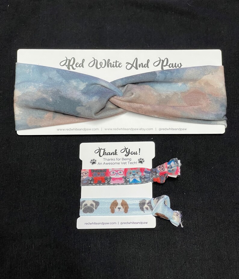 May include: A set of two colorful hair ties with a dog print design. The hair ties are packaged on a white card with the text "Red White And Paw" and "Thank You! Thanks for Being An Awesome Vet Tech!" The card also includes the website address "redwhiteandpaw.com" and the social media handle "@redwhiteandpaw".