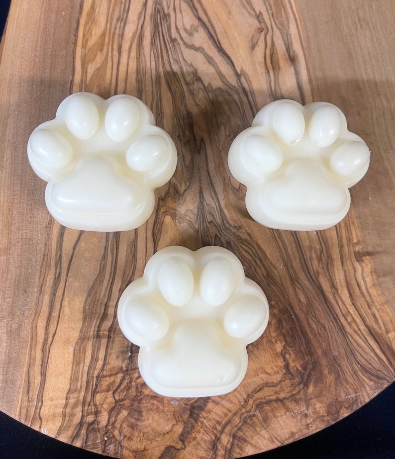 May include: Three white paw-shaped soaps on a wooden surface. The soaps are made in the shape of a dog's paw print.