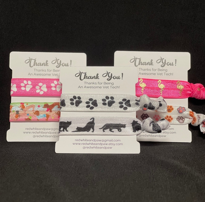Op de afbeelding: Drie bedankkaartjes met kleurrijke haarbandjes. De kaartjes hebben de tekst "Bedankt!" en zeggen "Bedankt dat je een geweldige dierenartsassistent bent!" De haarbandjes hebben pootjes, katten en flamingo's.