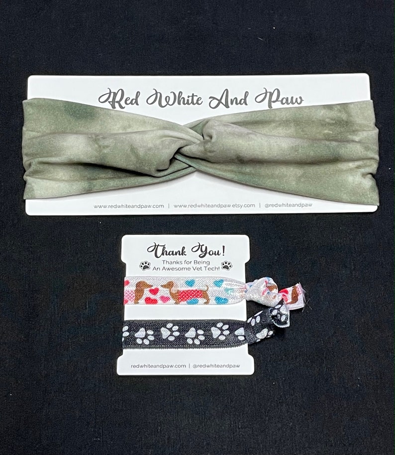 May include: A set of two hair scrunchies with a green and white tie-dye headband. The scrunchies feature a dachshund dog design with hearts and paw prints. The packaging includes the text "Red White And Paw" and "Thank You! Thanks for Being An Awesome Vet Tech!"