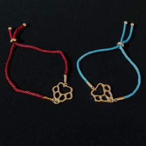 May include: Two adjustable bracelets with paw print charms. One bracelet is red and the other is blue.