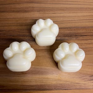 May include: Three white paw-shaped soaps on a wooden surface.