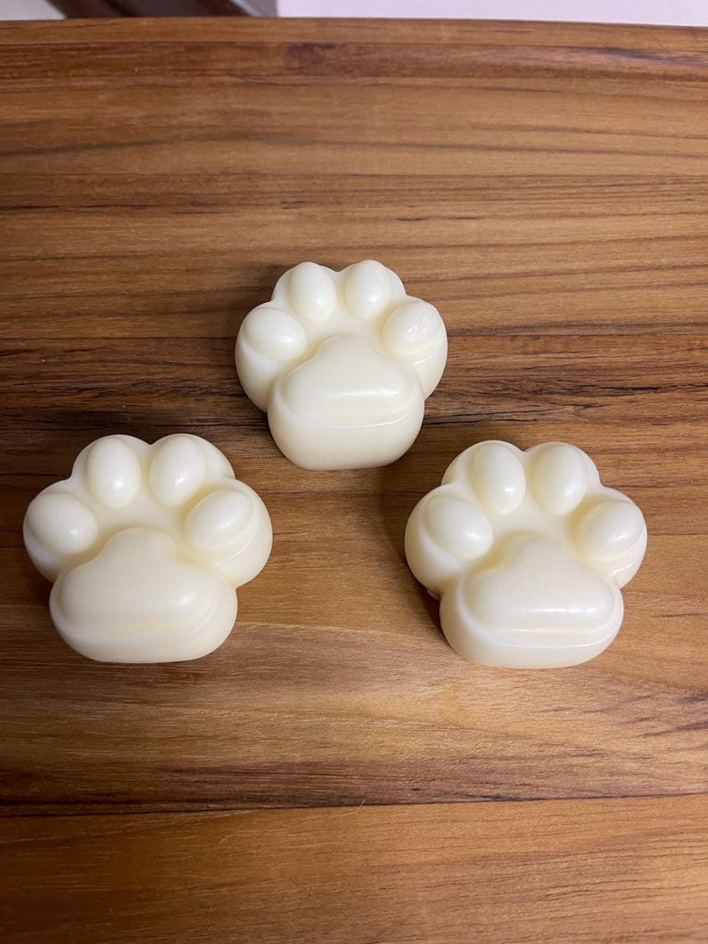 May include: Three white paw-shaped soaps on a wooden surface.