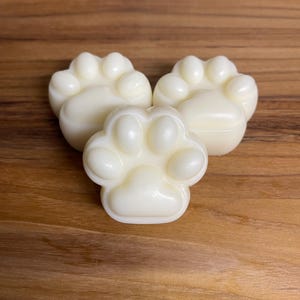 May include: Three white paw-shaped soaps on a wooden surface.