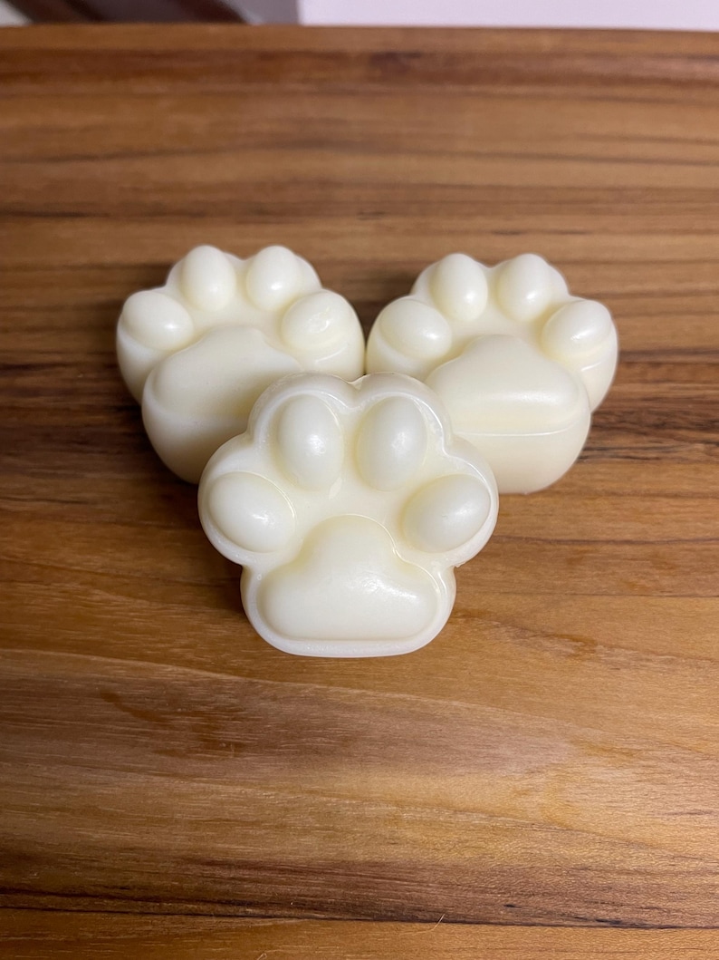 May include: Three white paw-shaped soaps on a wooden surface.