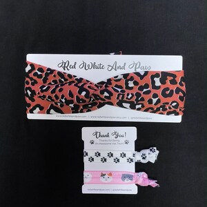 May include: A set of two hair scrunchies with a leopard print headband. The scrunchies feature paw prints and a cat design. The headband is red with black and white spots. The packaging includes the text "Red White And Paw" and "Thank You! Thanks for Being An Awesome Vet Tech!"
