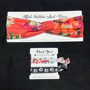 May include: A set of two hair scrunchies with a floral print and a paw print design. The scrunchies are packaged on a card with the text "Red White And Paw" and "Thank You! Thanks for Being An Awesome Vet Tech!"