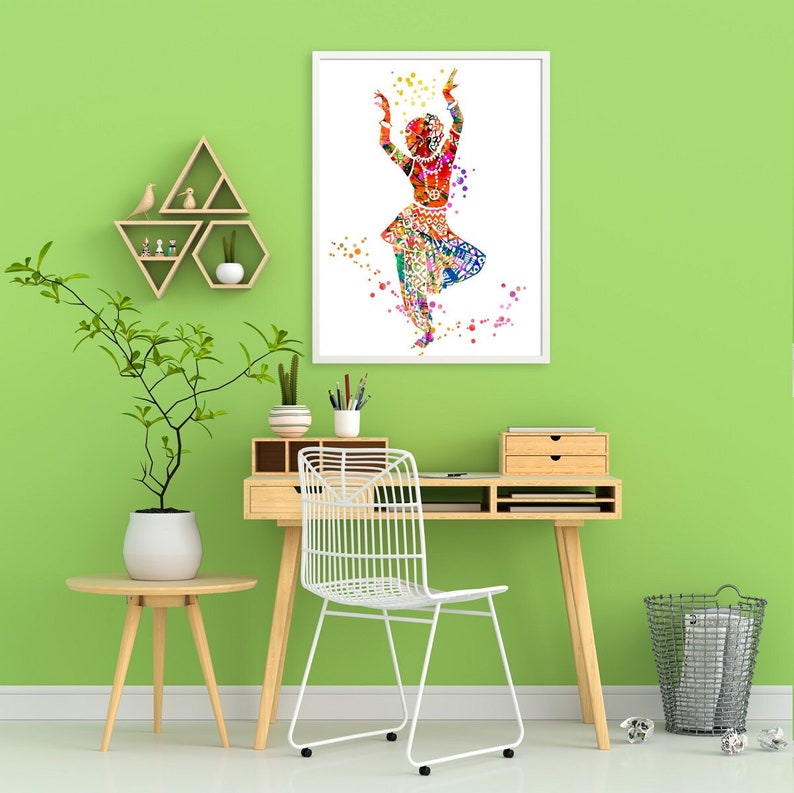 Puede incluir: Una pintura acuarela colorida de una mujer bailando. La pintura est&aacute; enmarcada en un marco blanco y est&aacute; colgada en una pared verde. La pared tambi&eacute;n tiene un estante de madera con una peque&ntilde;a figura de p&aacute;jaro y un escritorio con una silla blanca.