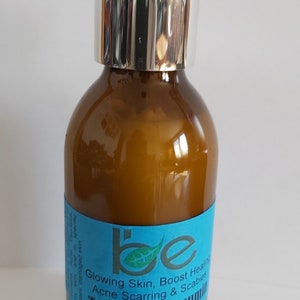 May include: A brown glass bottle with a silver pump top and a blue label that reads "be Glowing Skin, Boost Healing Acne Scarring & Scabies Turmeric Curcumin".