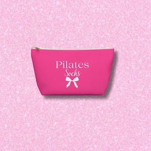 May include: A hot pink zippered pouch with a white bow and the text "Pilates Socks" printed on it.