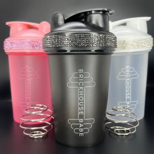 May include: Three black, pink, and white shaker bottles with a silver metal mixing ball. Each bottle has a black and white logo that says "Brickhouse Babe" and a silver, sparkly band around the top.