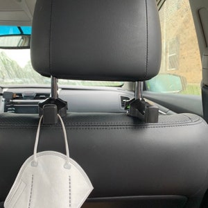 May include: A black car headrest hook with a white face mask hanging from it.
