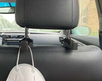 May include: A black car headrest hook with a white face mask hanging from it.