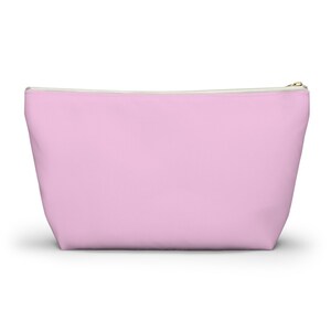 May include: A light pink zippered pouch with a white zipper.