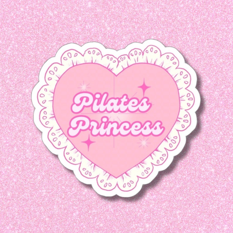 May include: A pink sticker in the shape of a heart with the words "Pilates Princess" in a retro font. The heart is outlined with a white, scalloped border and adorned with starburst accents, set against a glittery pink background.