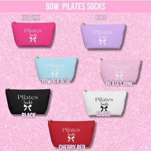May include: Six different colored zippered pouches with the text "Pilates Socks" and a white bow printed on them. The pouches are in the colors hot pink, lilac, powder blue, black, white, and cherry red.