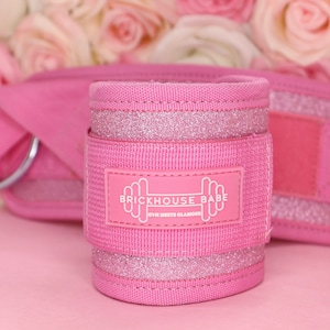 May include: Pink ankle weights with glitter accents and a white logo that reads "Brickhouse Babe Gym Meets Glamour".