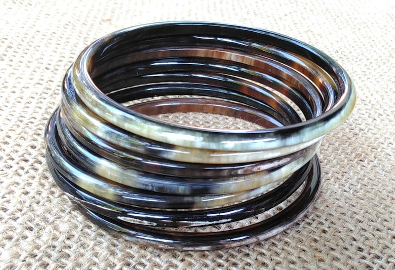 May include: A stack of horn bangles in black, brown, and cream colors. The bangles are stacked in a spiral shape.