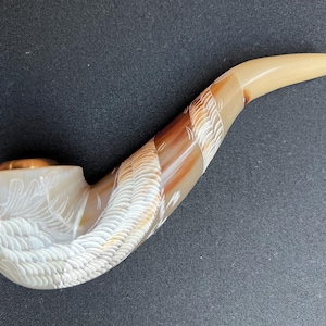 May include: A white and brown carved pipe with a dragon design. The pipe is made of bone or horn and has a small bowl at the end.