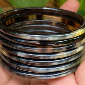 May include: A set of eight horn bangles in black and white with a glossy finish. The bangles are stacked on top of each other.