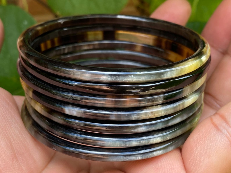May include: A set of eight horn bangles in black and white with a glossy finish. The bangles are stacked on top of each other.