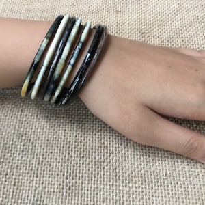 May include: A set of black and white patterned bangles. The bangles are made of a hard, smooth material and are stacked on a person's wrist.