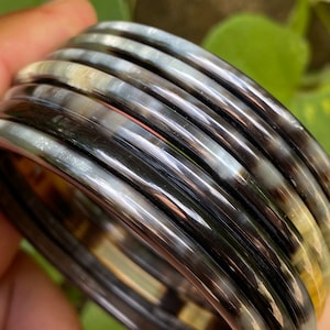 May include: A set of black and white horn bangles. The bangles are stacked on top of each other and have a shiny finish.