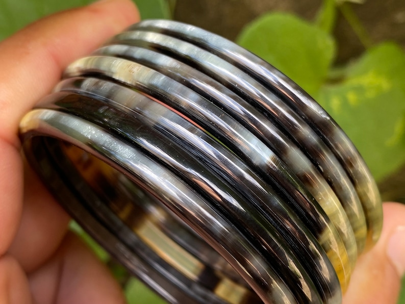 May include: A set of black and white horn bangles. The bangles are stacked on top of each other and have a shiny finish.