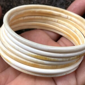 May include: A set of ivory bangles, stacked and arranged in a circular pattern. The bangles are a creamy white color with a slight yellow hue.