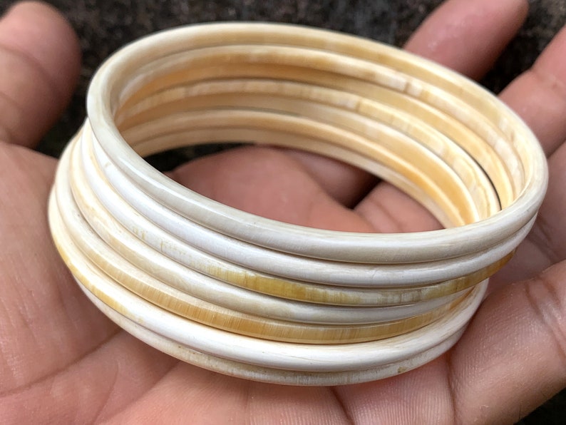 May include: A set of ivory bangles, stacked and arranged in a circular pattern. The bangles are a creamy white color with a slight yellow hue.