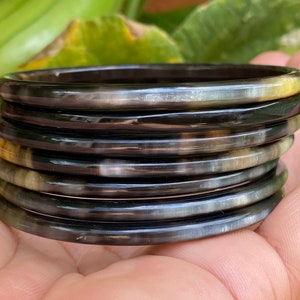 May include: A stack of eight black and brown horn bangles. The bangles are smooth and shiny, and they are stacked on top of each other.
