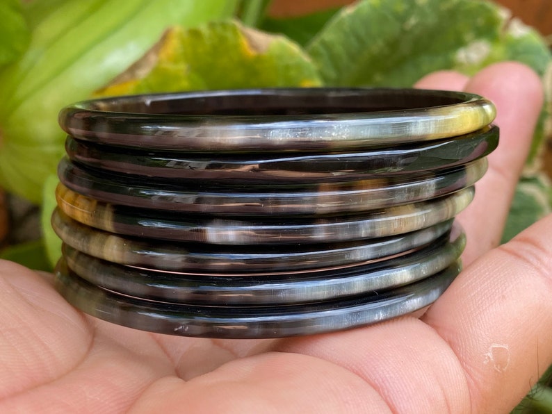 May include: A stack of eight black and brown horn bangles. The bangles are smooth and shiny, and they are stacked on top of each other.