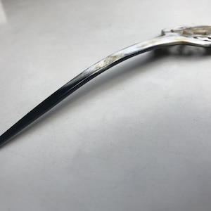 May include: A long, black and white hair stick with a decorative, openwork design at the top.