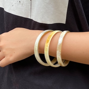 Peut inclure: Trois bracelets en ivoire empilés sur le poignet d'une personne. Les bracelets sont faits d'un matériau lisse et poli et ont un éclat naturel subtil.