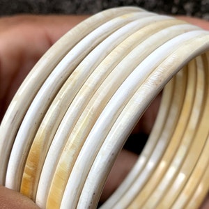 May include: A set of six ivory-colored bangles, stacked and arranged in a circular pattern. The bangles are smooth and polished, with a slight sheen.