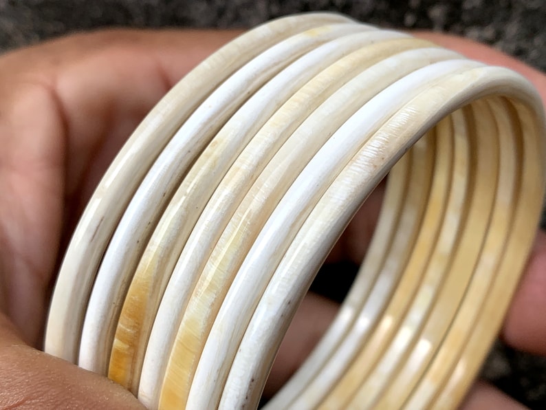 May include: A set of six ivory-colored bangles, stacked and arranged in a circular pattern. The bangles are smooth and polished, with a slight sheen.