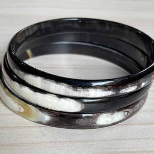 May include: Three black and white horn bangles stacked on top of each other. The bangles are made of polished horn and have a natural, organic look.