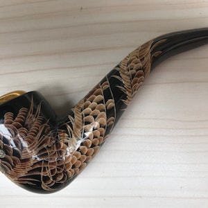 May include: A black and brown wooden pipe with a dragon design. The pipe has a gold-colored metal band around the bowl.