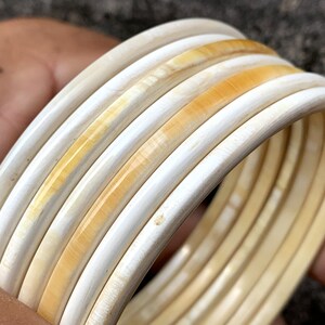 May include: A set of six ivory-colored bangles with a subtle yellow hue. The bangles are stacked on top of each other, creating a layered effect.