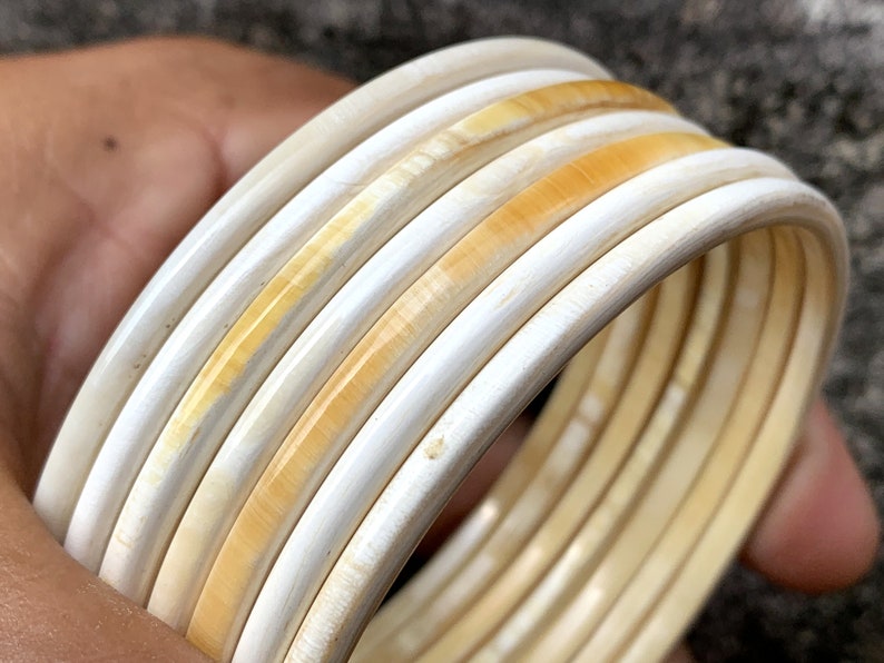 May include: A set of six ivory-colored bangles with a subtle yellow hue. The bangles are stacked on top of each other, creating a layered effect.