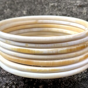 May include: A set of ivory bangles, stacked and arranged in a circular pattern. The bangles are a creamy white color with a subtle yellow hue.