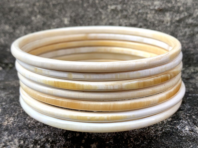 May include: A set of ivory bangles, stacked and arranged in a circular pattern. The bangles are a creamy white color with a subtle yellow hue.