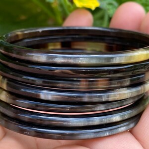 May include: A stack of eight black and white horn bangles. The bangles are smooth and shiny, and they have a natural, organic look.