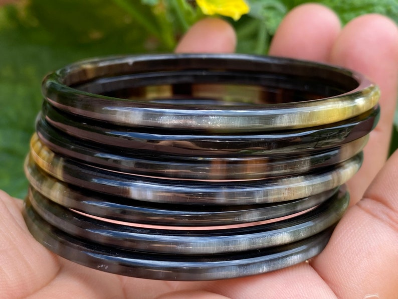 May include: A stack of eight black and white horn bangles. The bangles are smooth and shiny, and they have a natural, organic look.