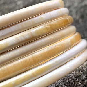 May include: A set of six ivory and cream colored bangle bracelets. The bracelets are stacked on top of each other, creating a layered effect.
