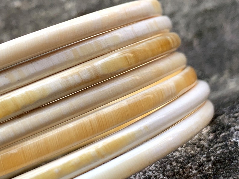May include: A set of six ivory and cream colored bangle bracelets. The bracelets are stacked on top of each other, creating a layered effect.